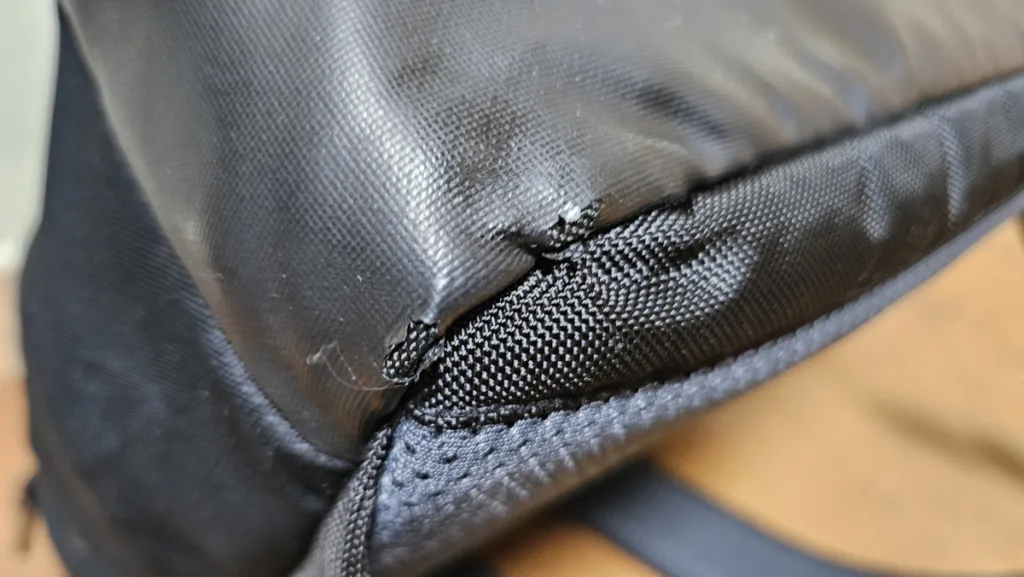 가방 아래 모서리 부분의 인조 가죽이 손상되어 내부 천이 드러난 모습